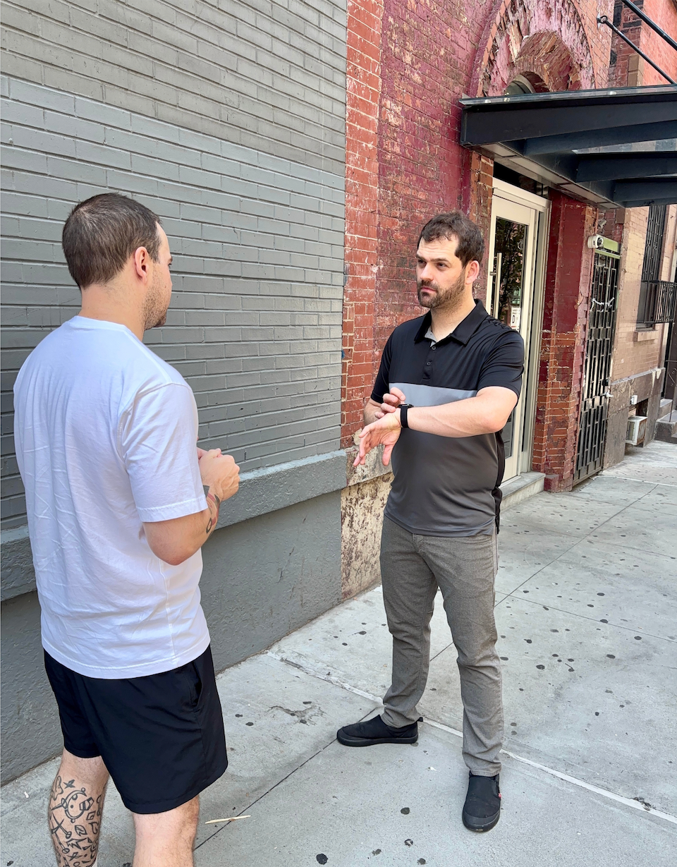 Edwin standing on a sidewalk mid-conversation, glancing at the Apple Watch on his wrist.