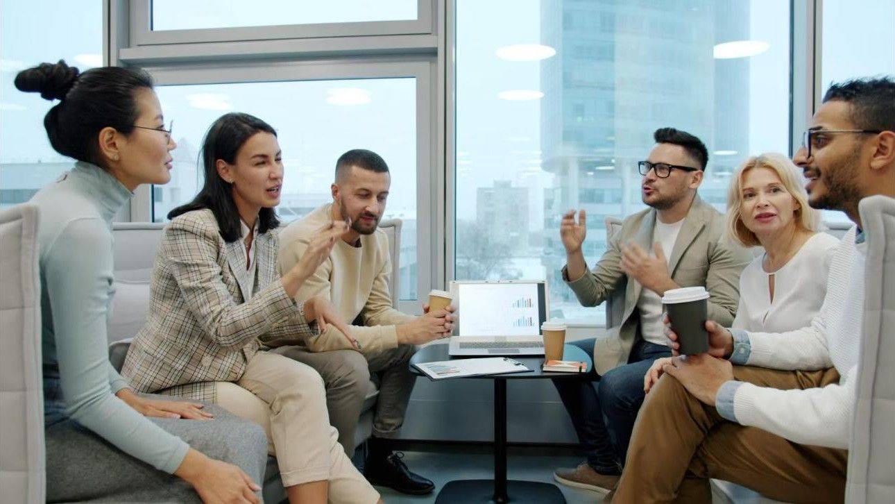 Diverse group of colleagues having a lively conversation around a laptop in a bright office