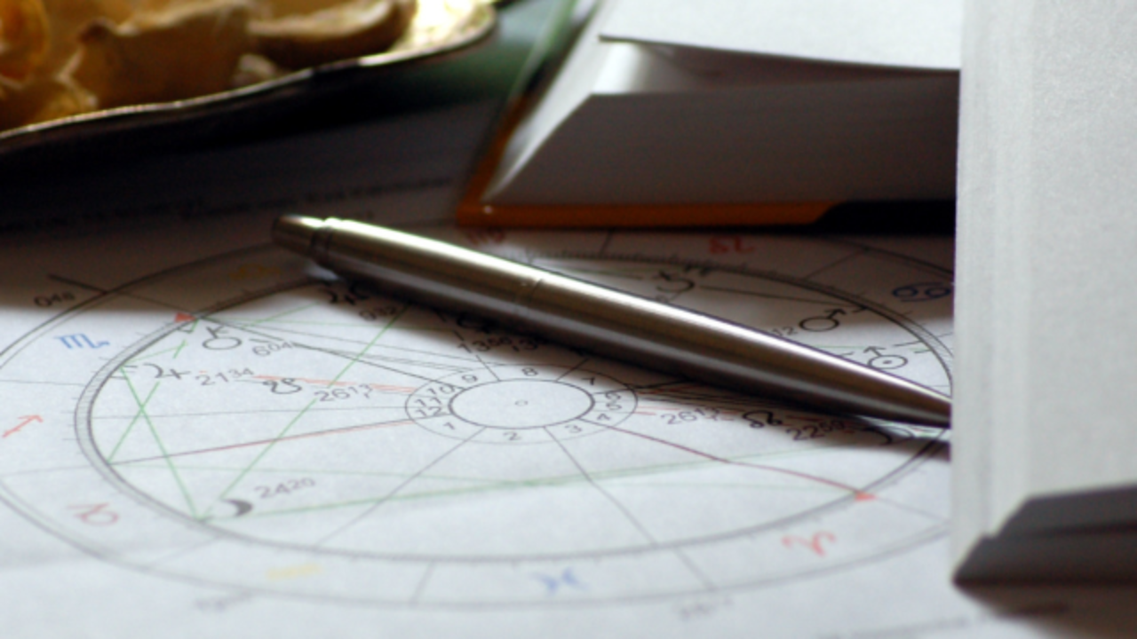 A beautifully designed natal (birth) chart printed on white paper alongside a notebook, a silver pen, in soft natural light.