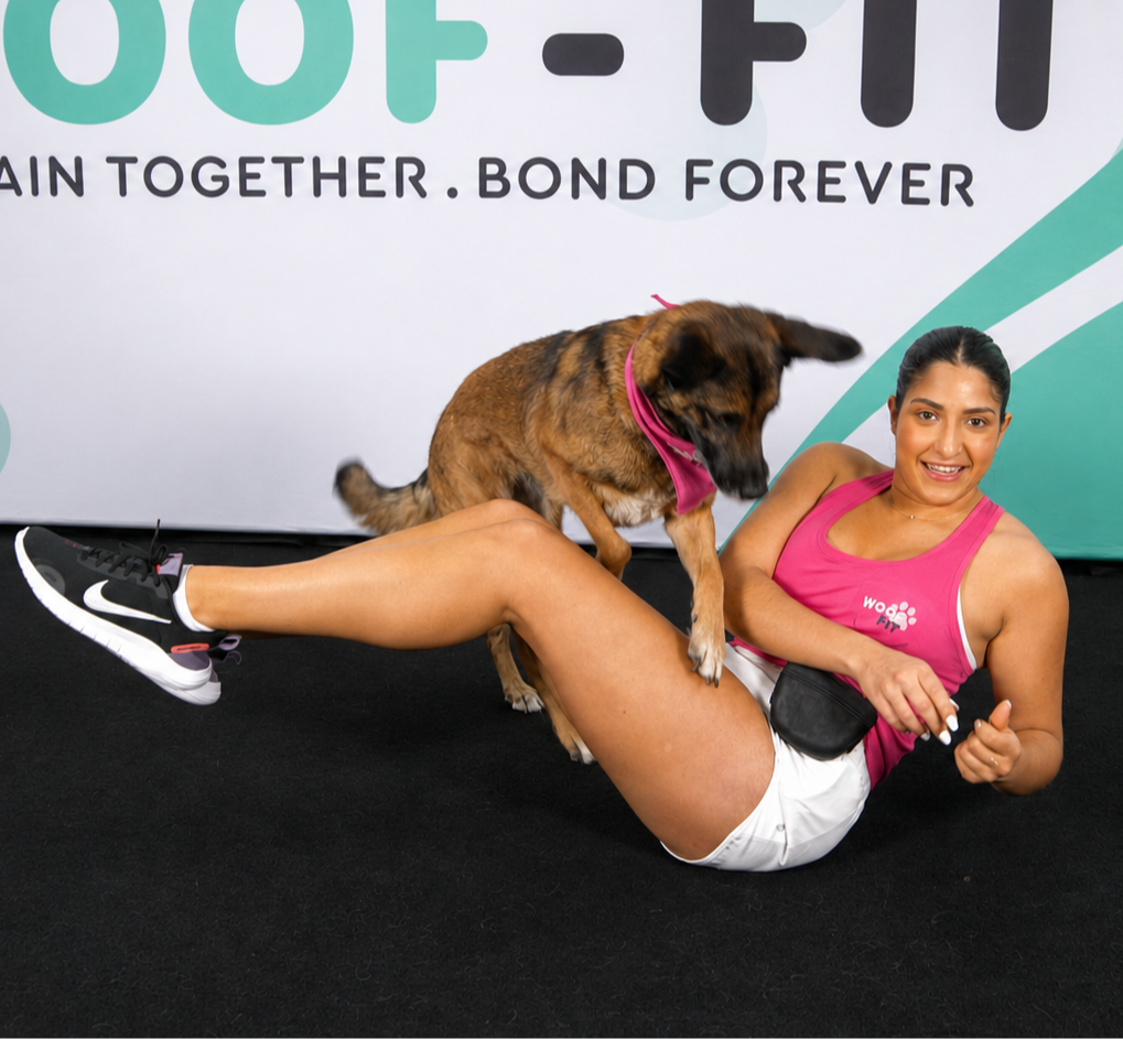 Woman doing a Russian-twist exercise while rewarding her Goldendoodle for jumping over her legs with a treat during a Woof-Fit workout