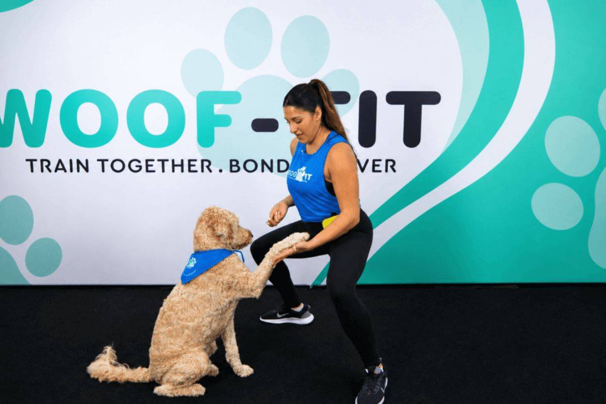 Woman holding a squat while asking her Goldendoodle for a paw and rewarding her with a treat during the Flow & Challenge workout