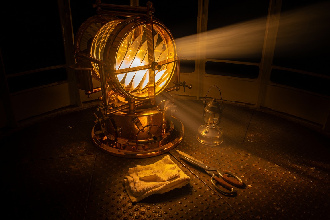 The great lamp of a lighthouse lit in its lantern room, a cloth and tools left beside it