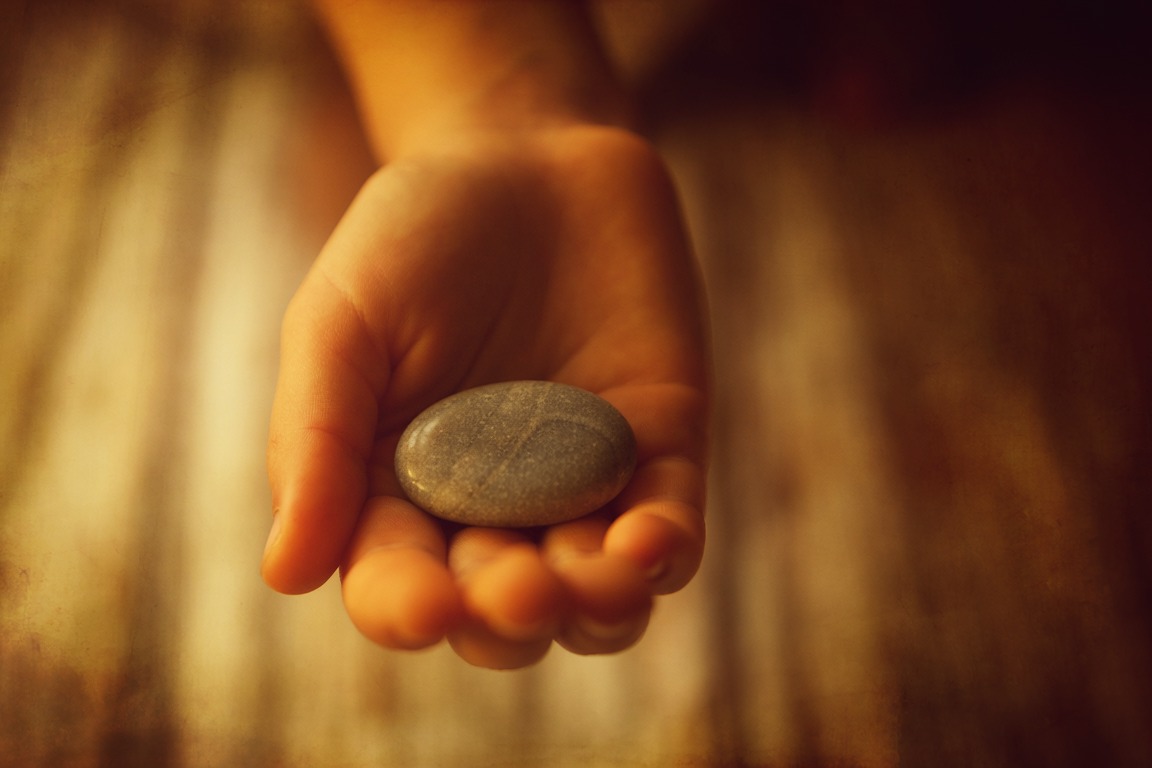 An open hand holding a small smooth stone