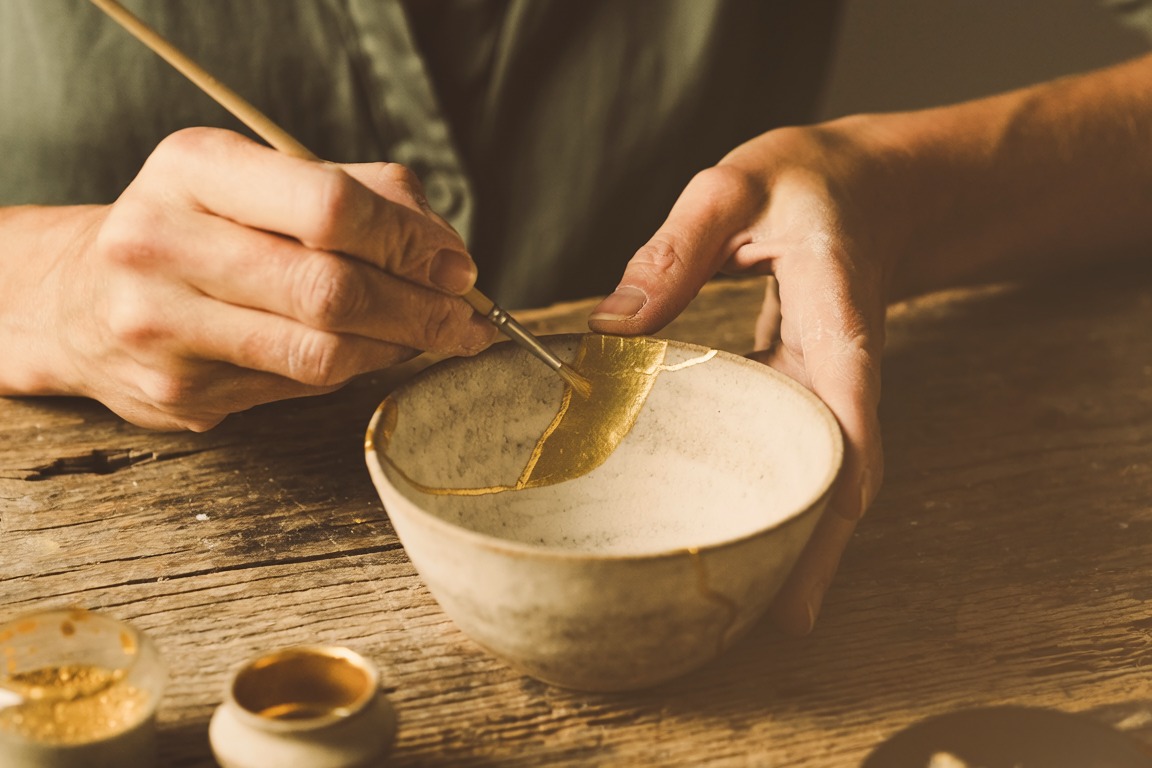 Two hands mending a cracked bowl with a fine brush