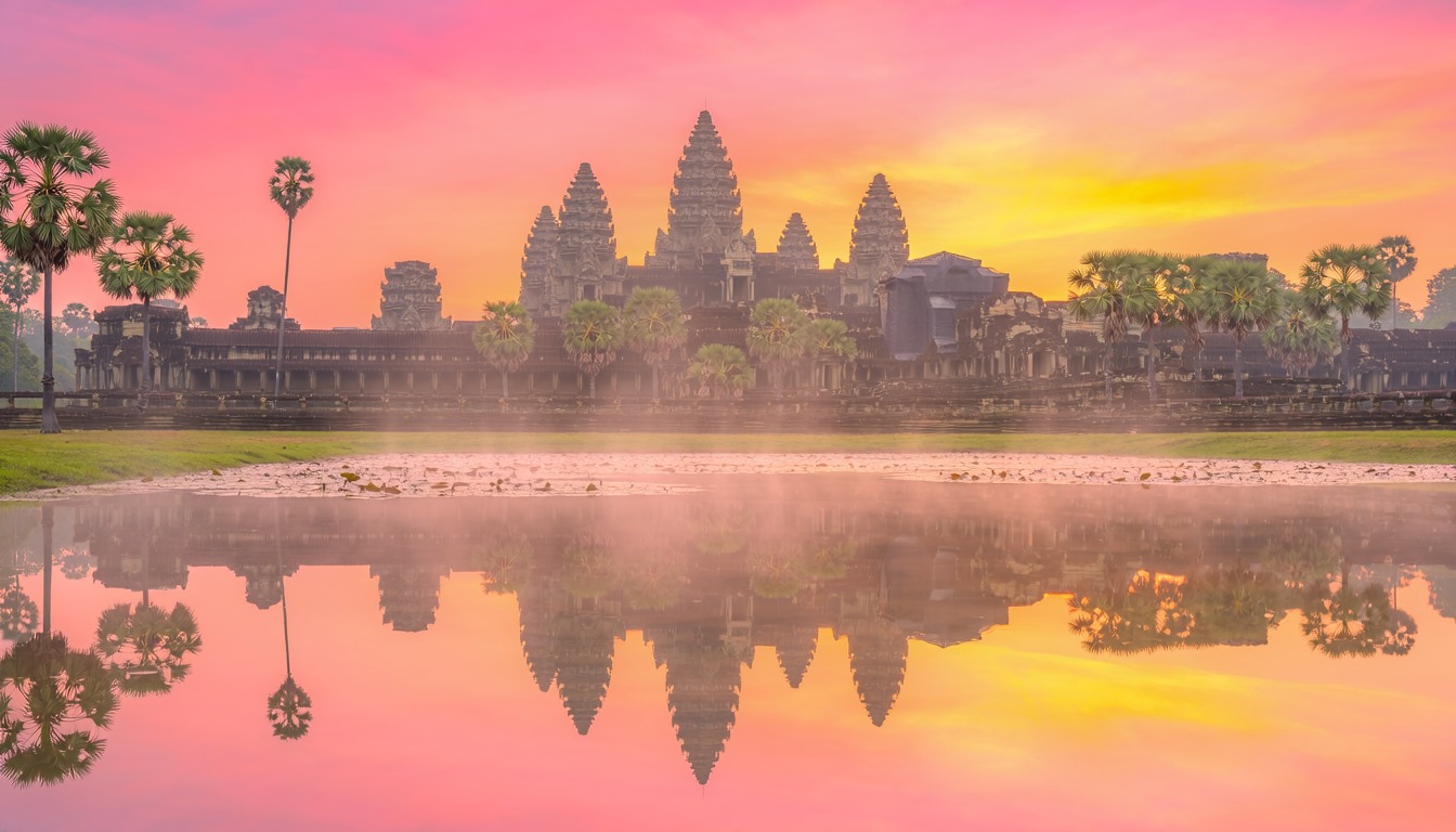 Angkor Wat at sunrise, its towers reflected in a still moat under a pink and gold sky