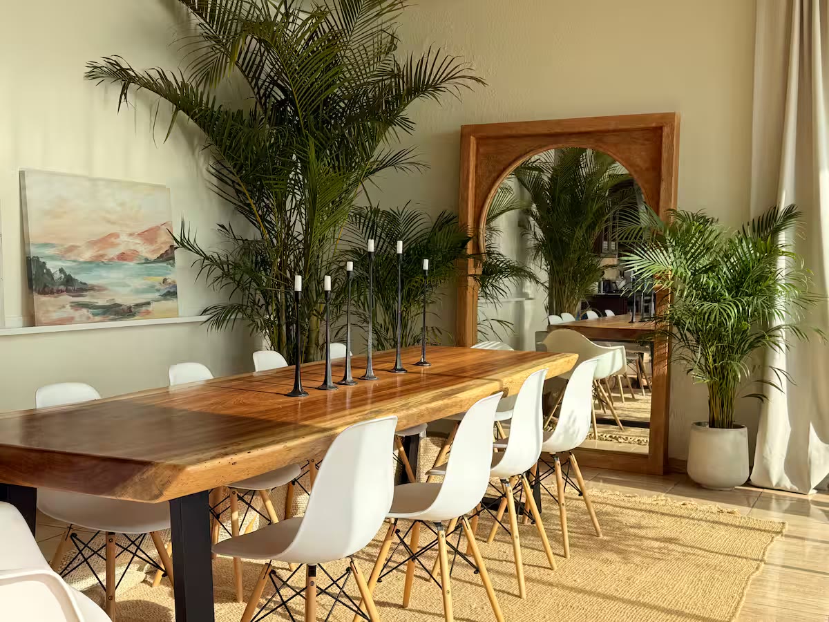 A long wooden dining table with candles and palms, set for shared meals