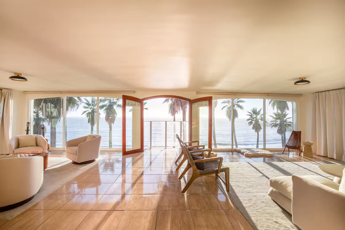 Bright living room with floor-to-ceiling windows opening onto palms and the ocean