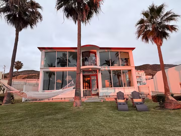 The house at golden hour, framed by palms, with a hammock and lounge chairs on the lawn