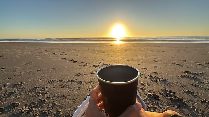 Holding a warm cup on the sand as the sun rises over the ocean
