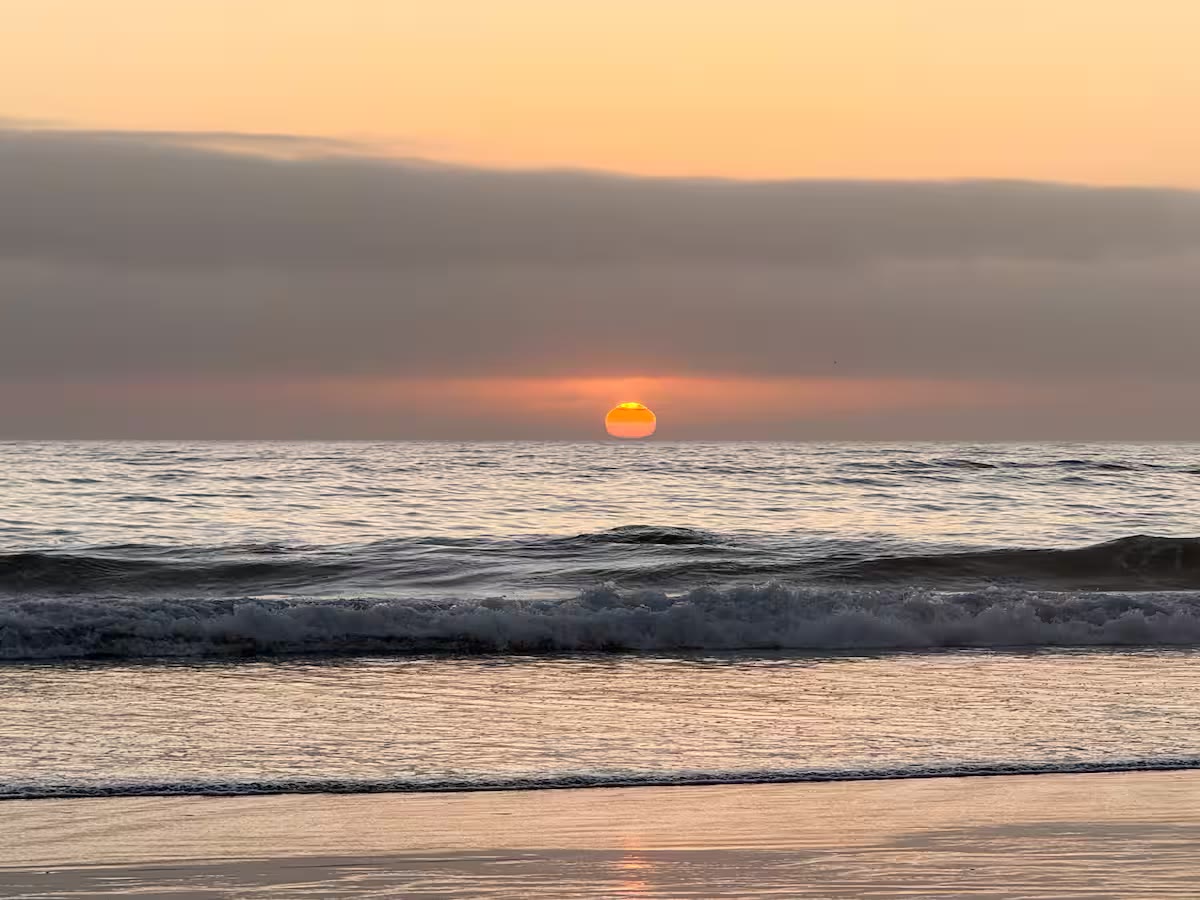 The sun setting into the ocean beneath a band of soft clouds