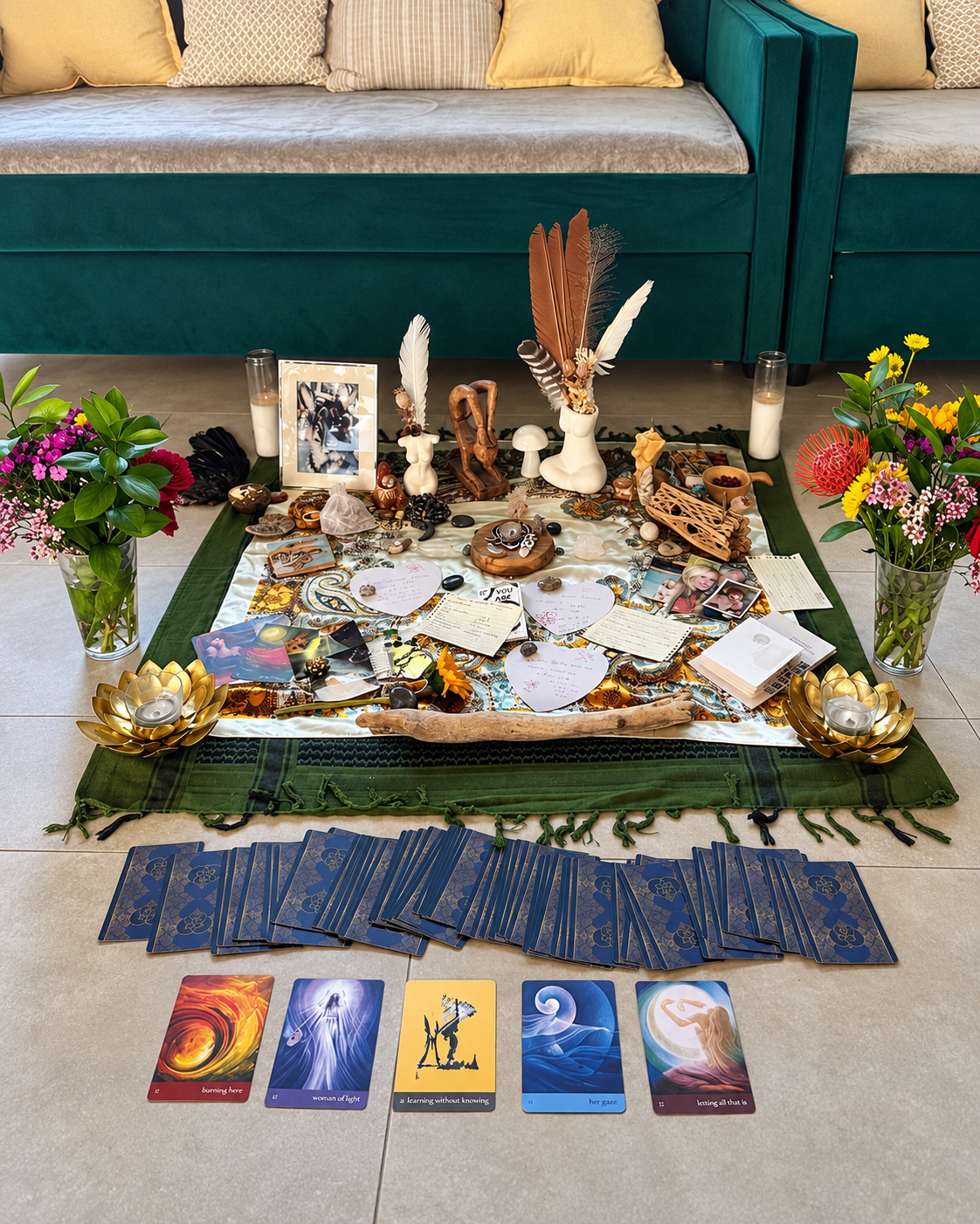 A ceremonial altar with feathers, candles, flowers, handwritten intentions and a spread of cards