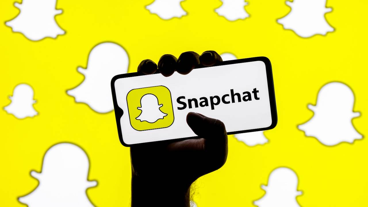 Graphic of snapchat logo on phone with snapchat icon wallpaper in the background