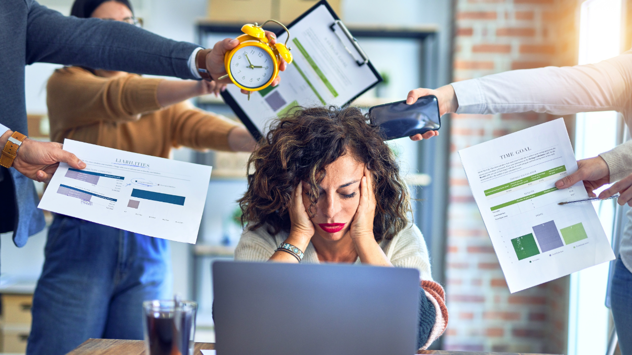 Employee overwhelmed with AI sitting at desk having a ton of things being handed to her. 