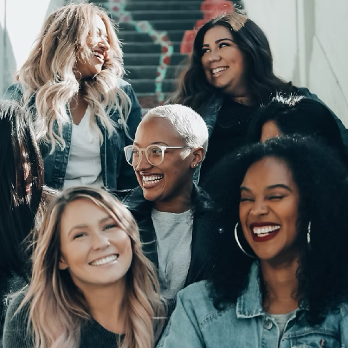 An image of 6 women sitting on a stairwell laughing and joking with each other.