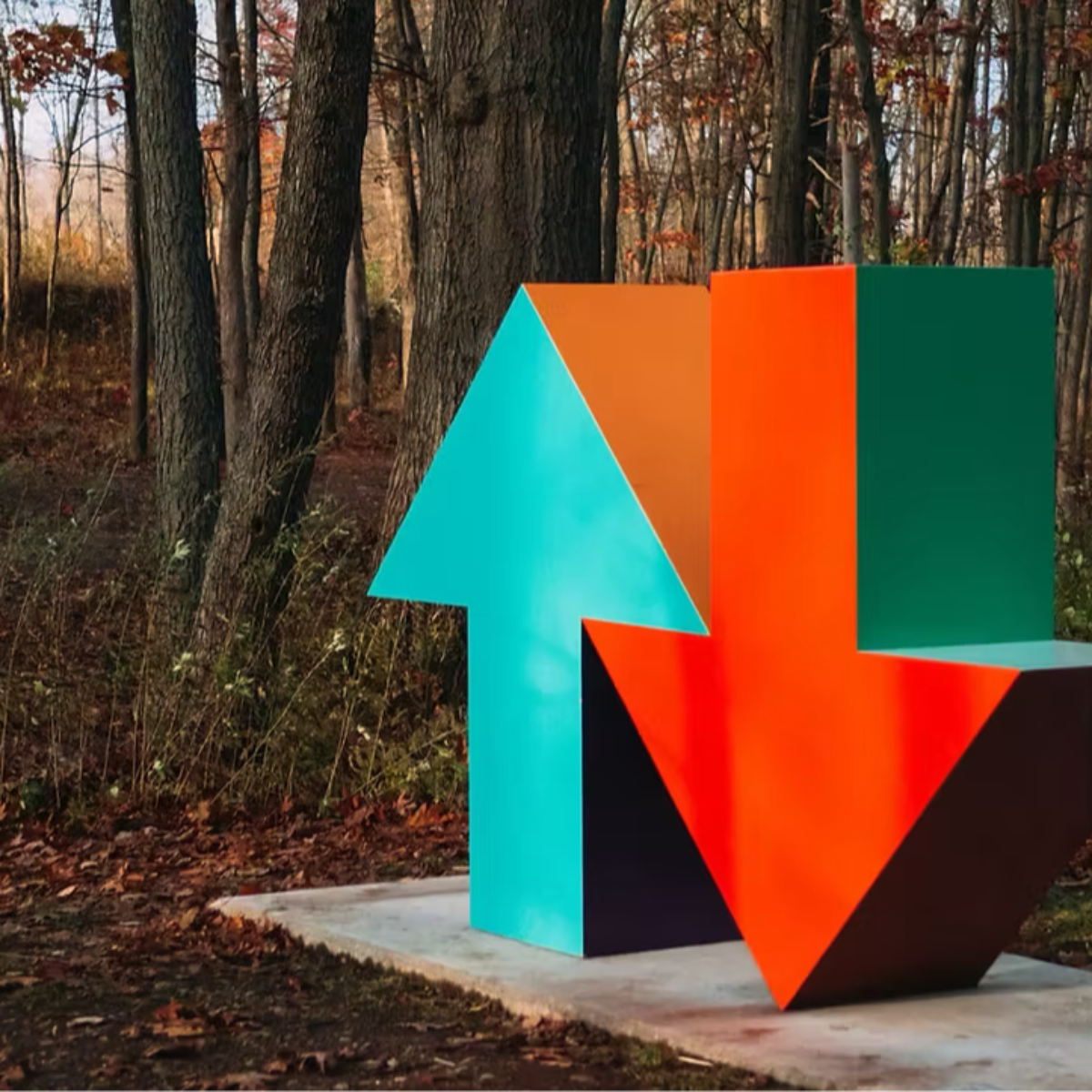 A sculpture in a forest. A blue arrow pointing upwards to the sky next to a red arrow pointing downwards into the ground.