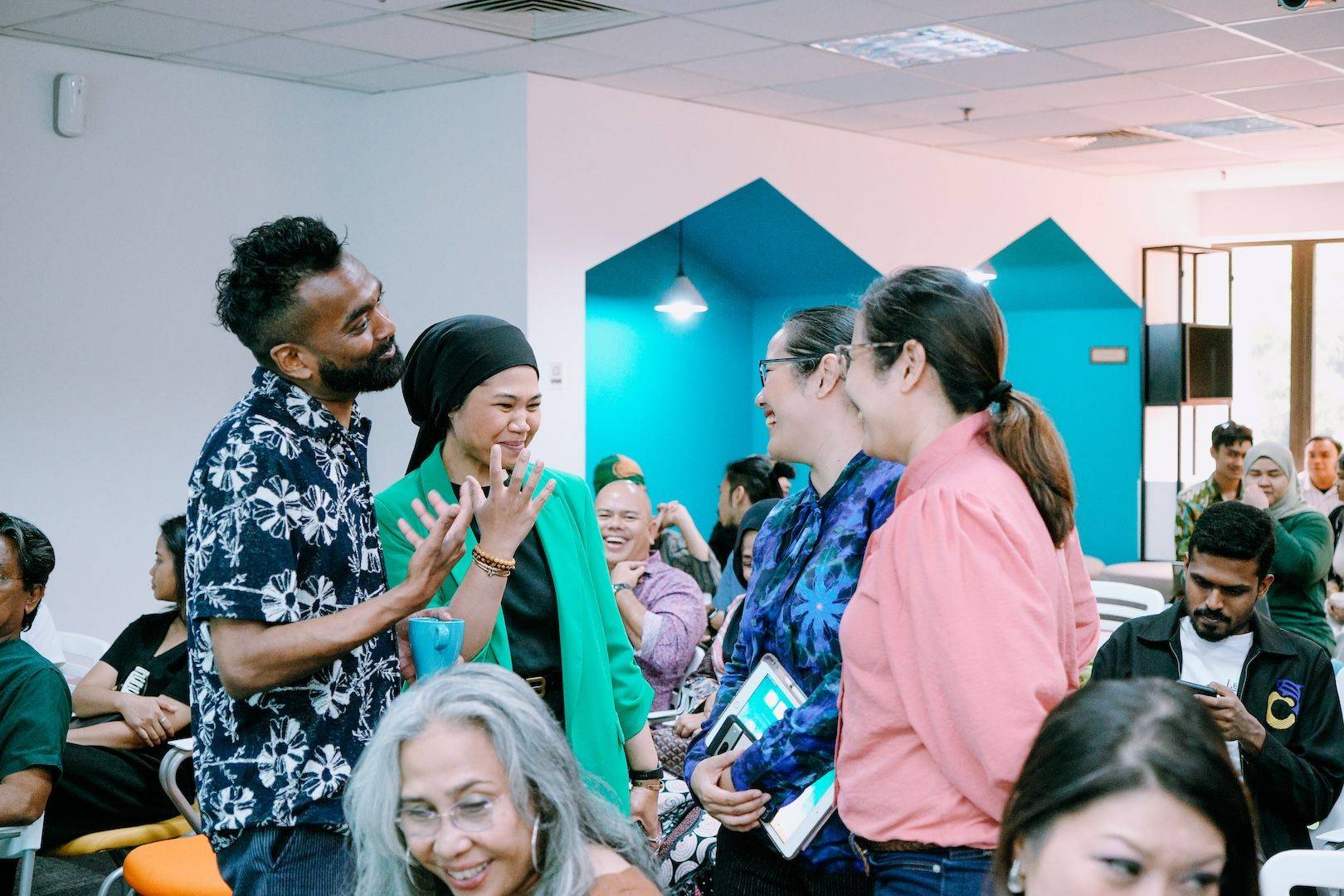 Rama Gheerawo leans into a lively conversation with a participant during an international workshop, listening with warmth as people around them smile, reflect and learn together.