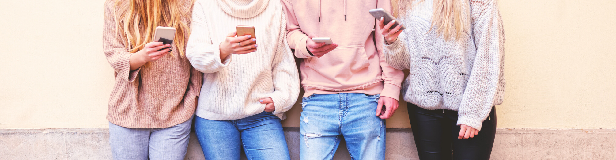 Vier jongeren tegen een muur met hun telefoon in de hand