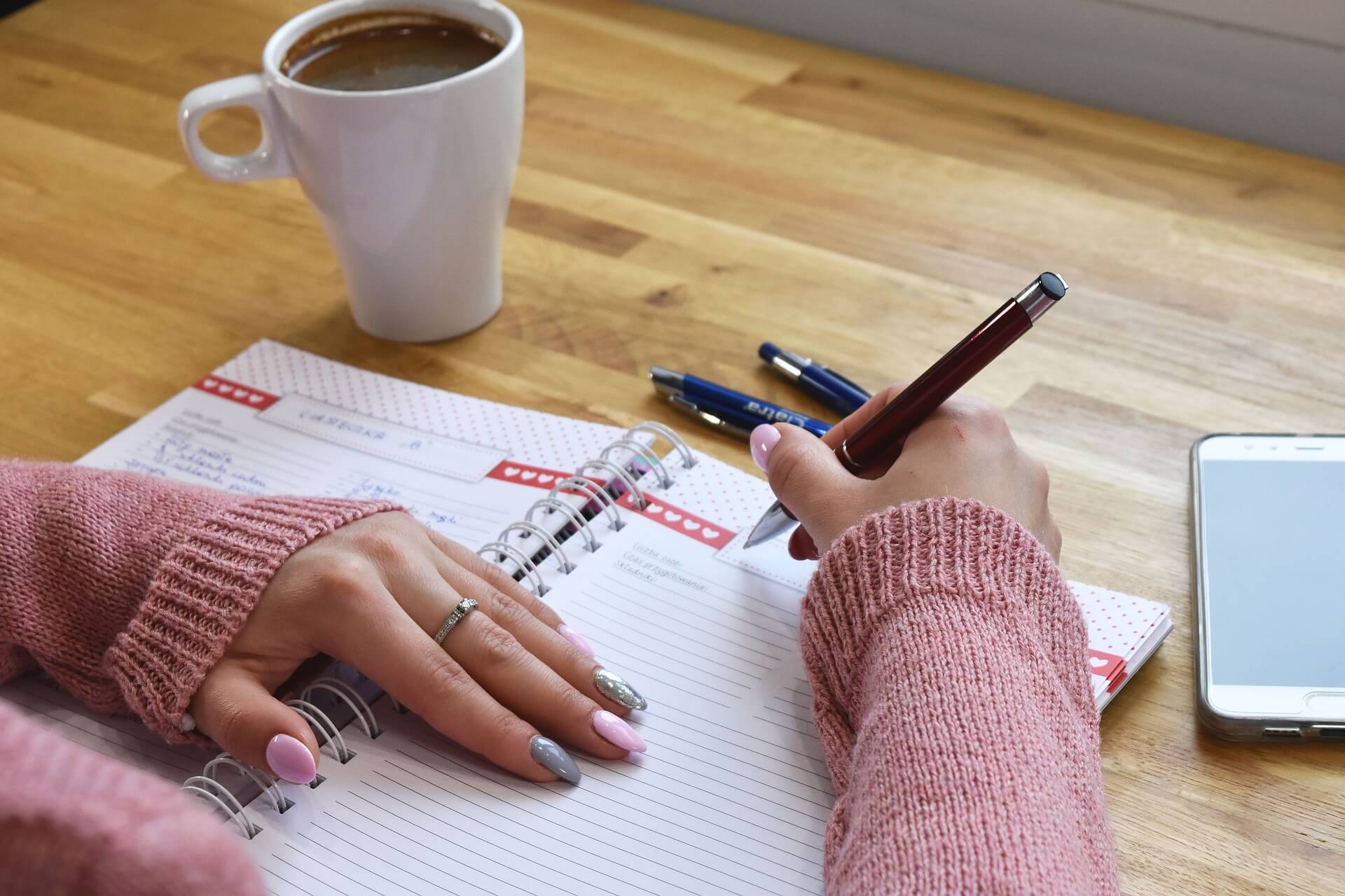 Handen die schrijven in een agenda, met een kop koffie ernaast