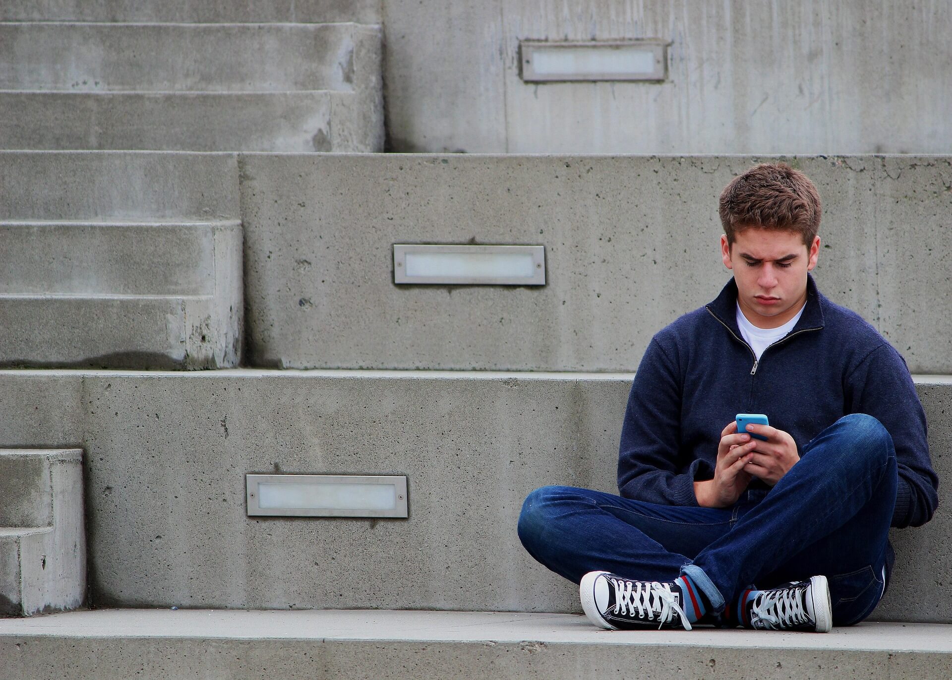 Jongen zit met zijn telefoon op een trap