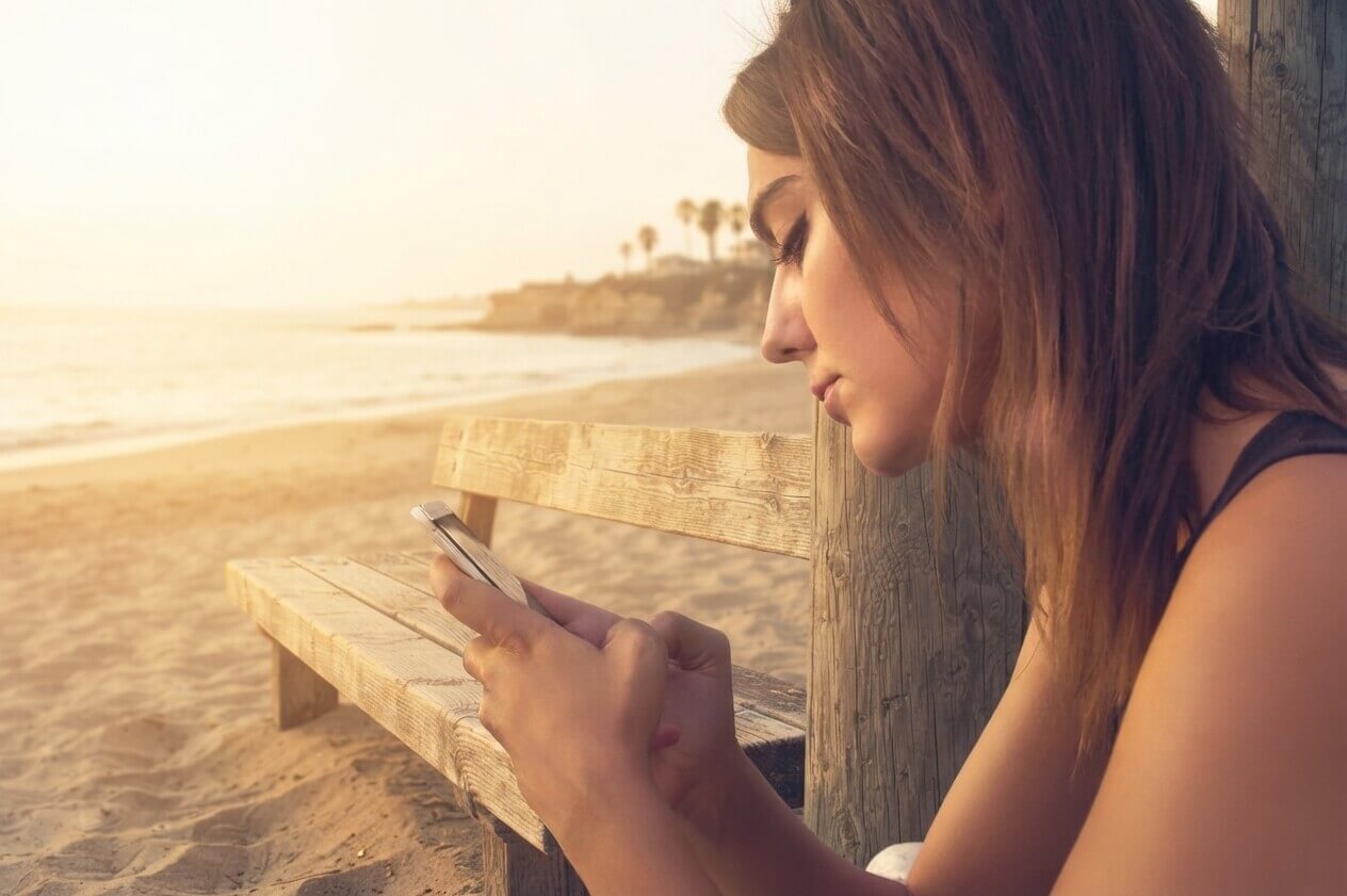 Tienermeisje met haar telefoon op het strand
