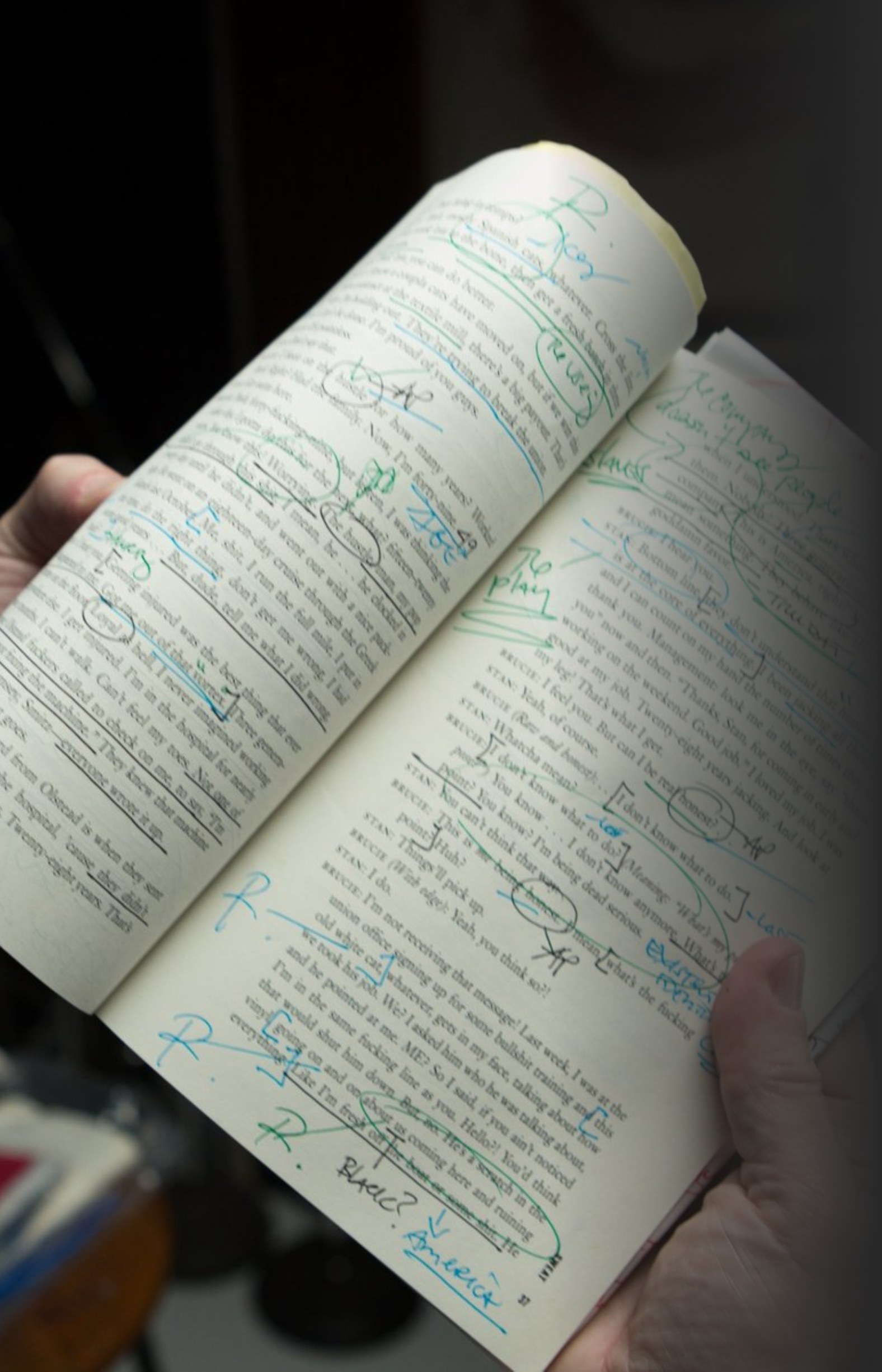 A hand holding a script covered in handwritten notes and underlines