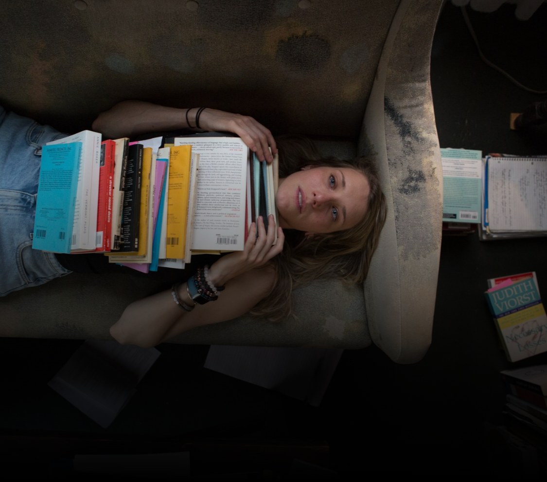 A woman lying on a sofa with a tall stack of plays on her chest