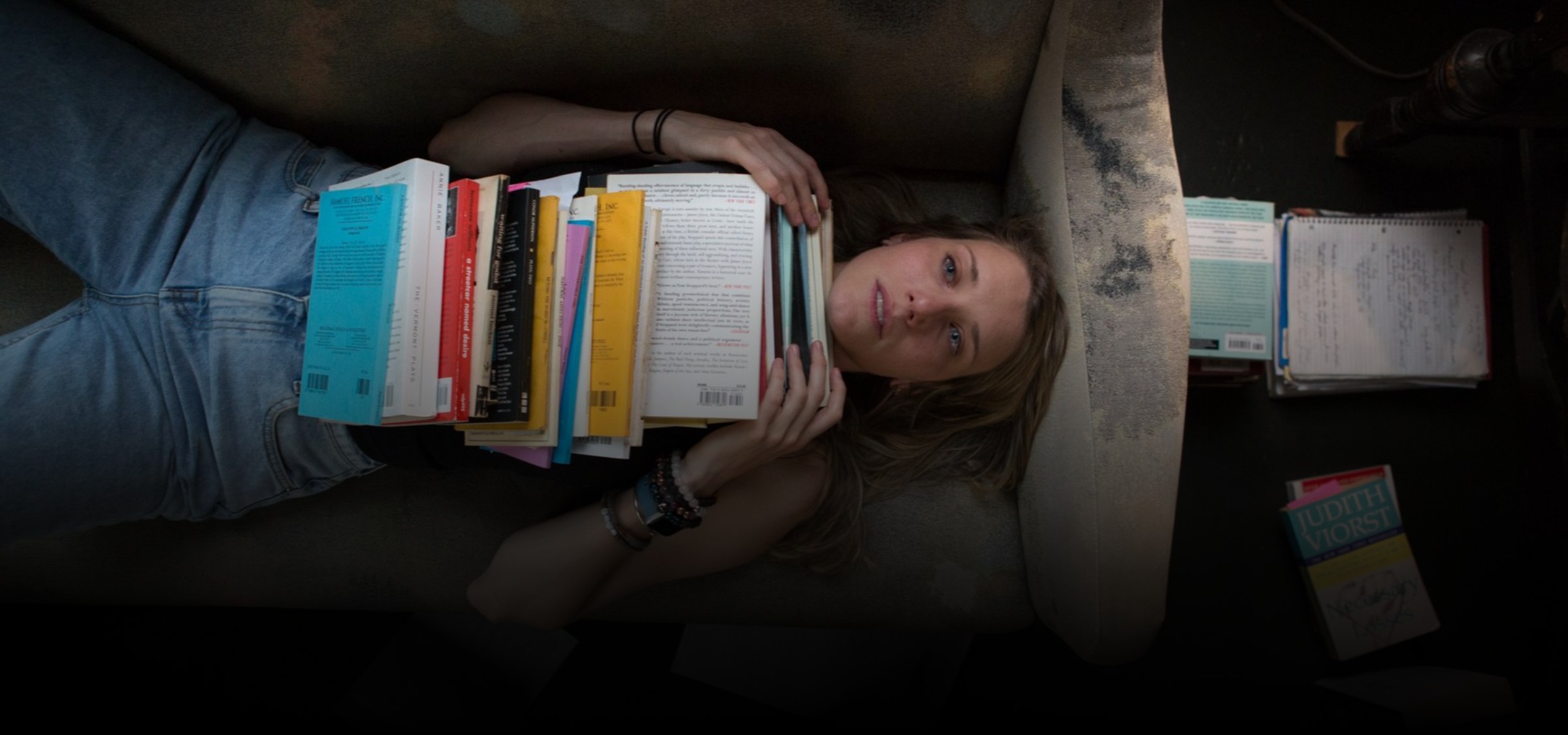 A woman lying on a sofa with a tall stack of plays on her chest