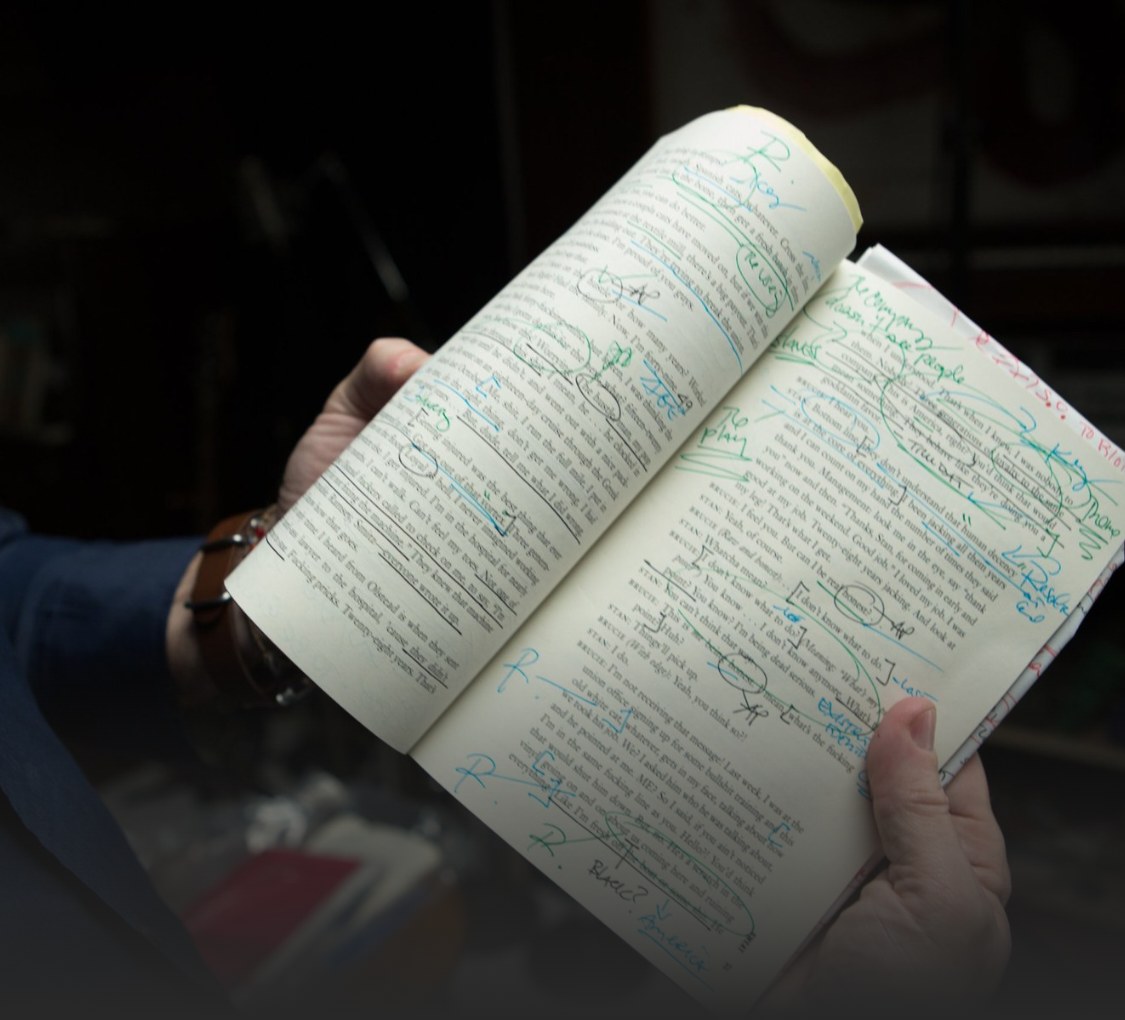 A hand holding a script covered in handwritten notes and underlines