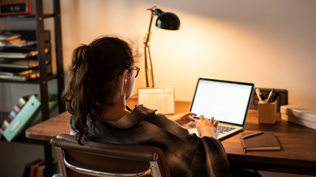 A teenager working at a laptop at a desk in the evening