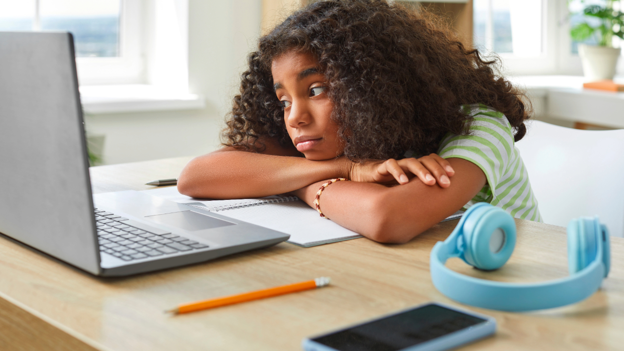 A teenager resting her head on her arms in front of a laptop