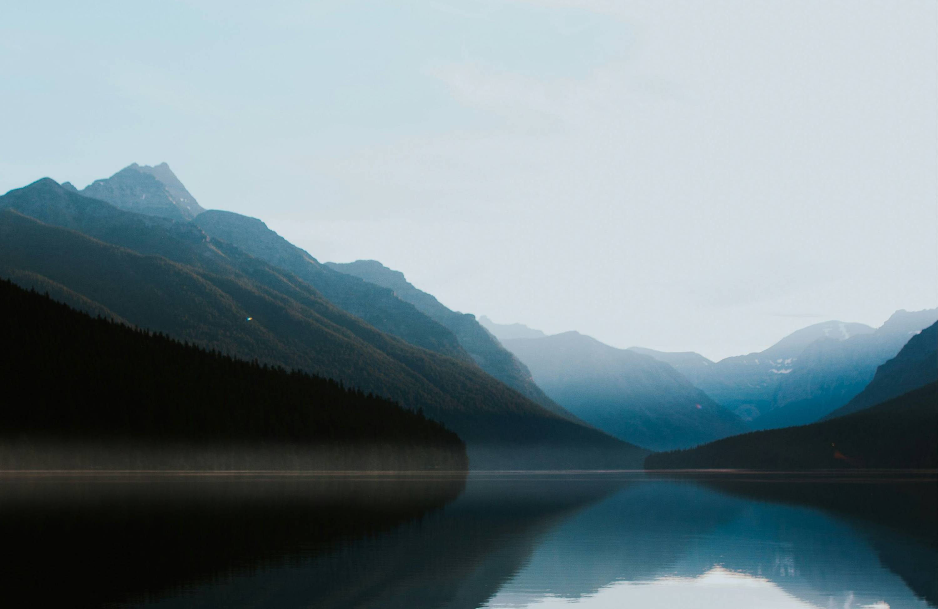 Mountain range reflected in a still lake beneath a soft blue sky.