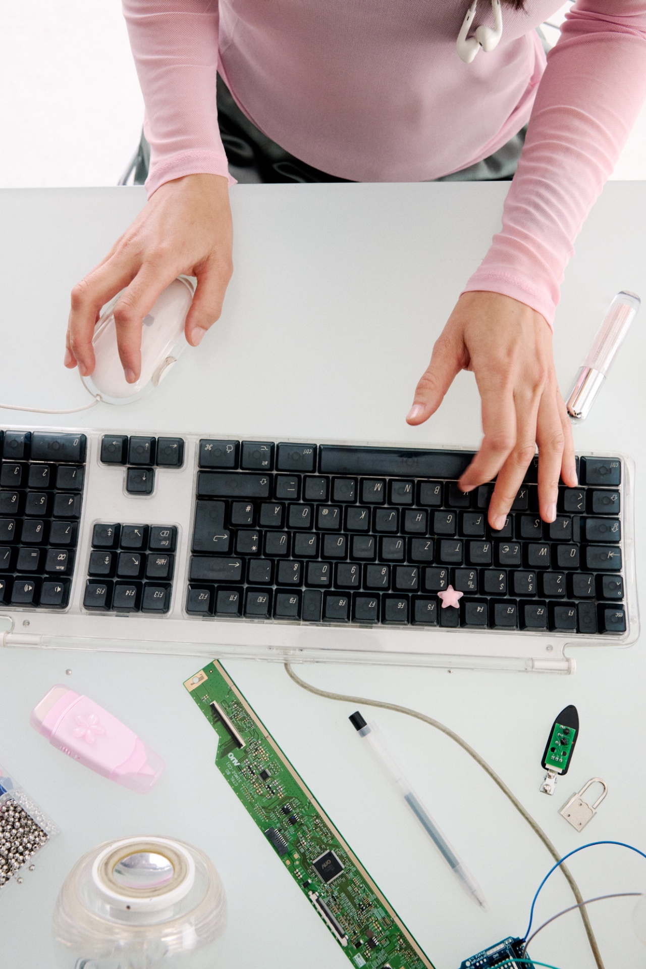 Hands typing on a keyboard surrounded by circuit boards and beauty tools