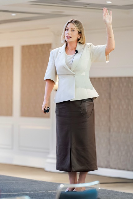 Tamara Reid on stage with her arm raised, presenting to a room