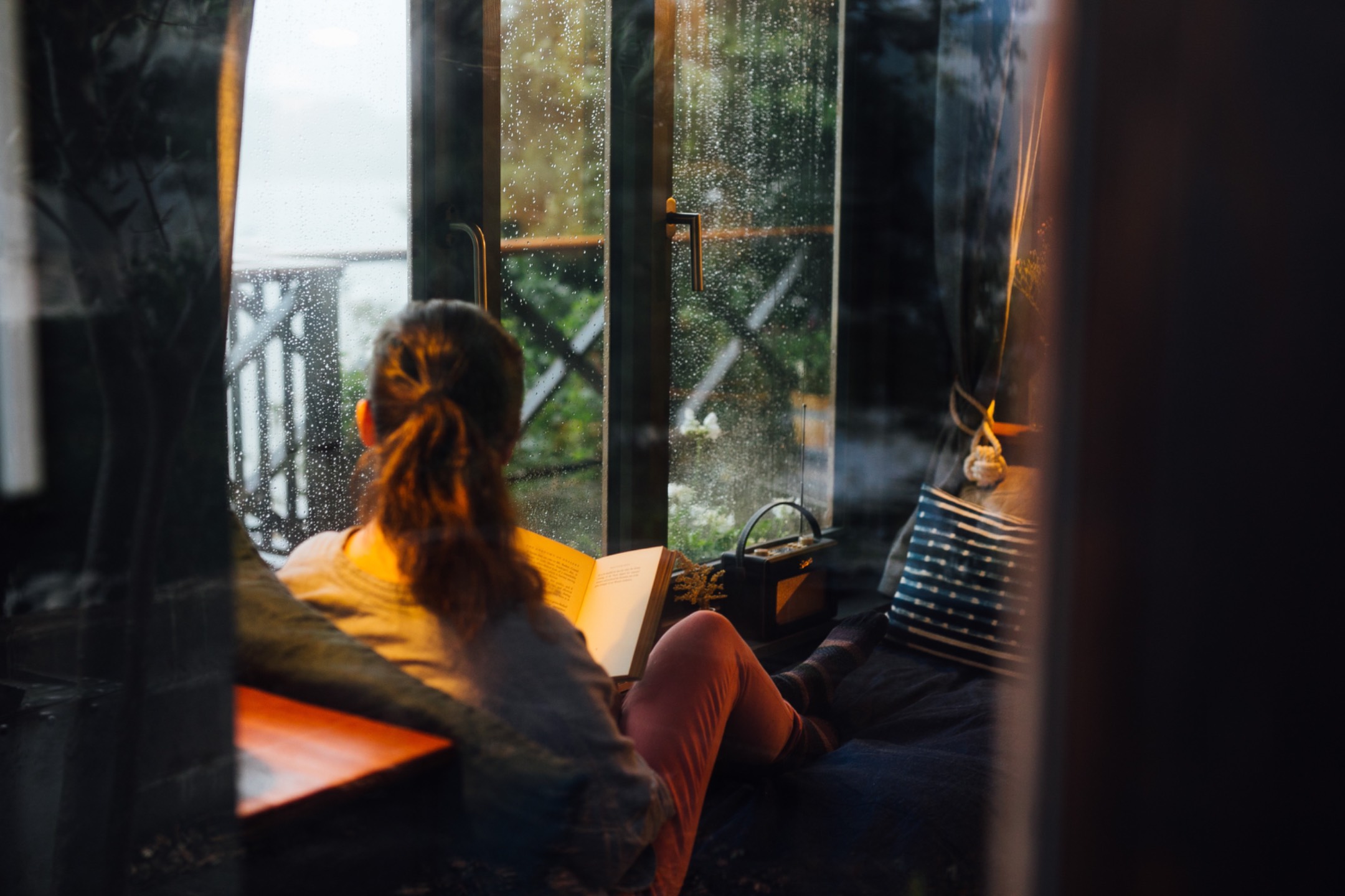A woman reading by a rainy window