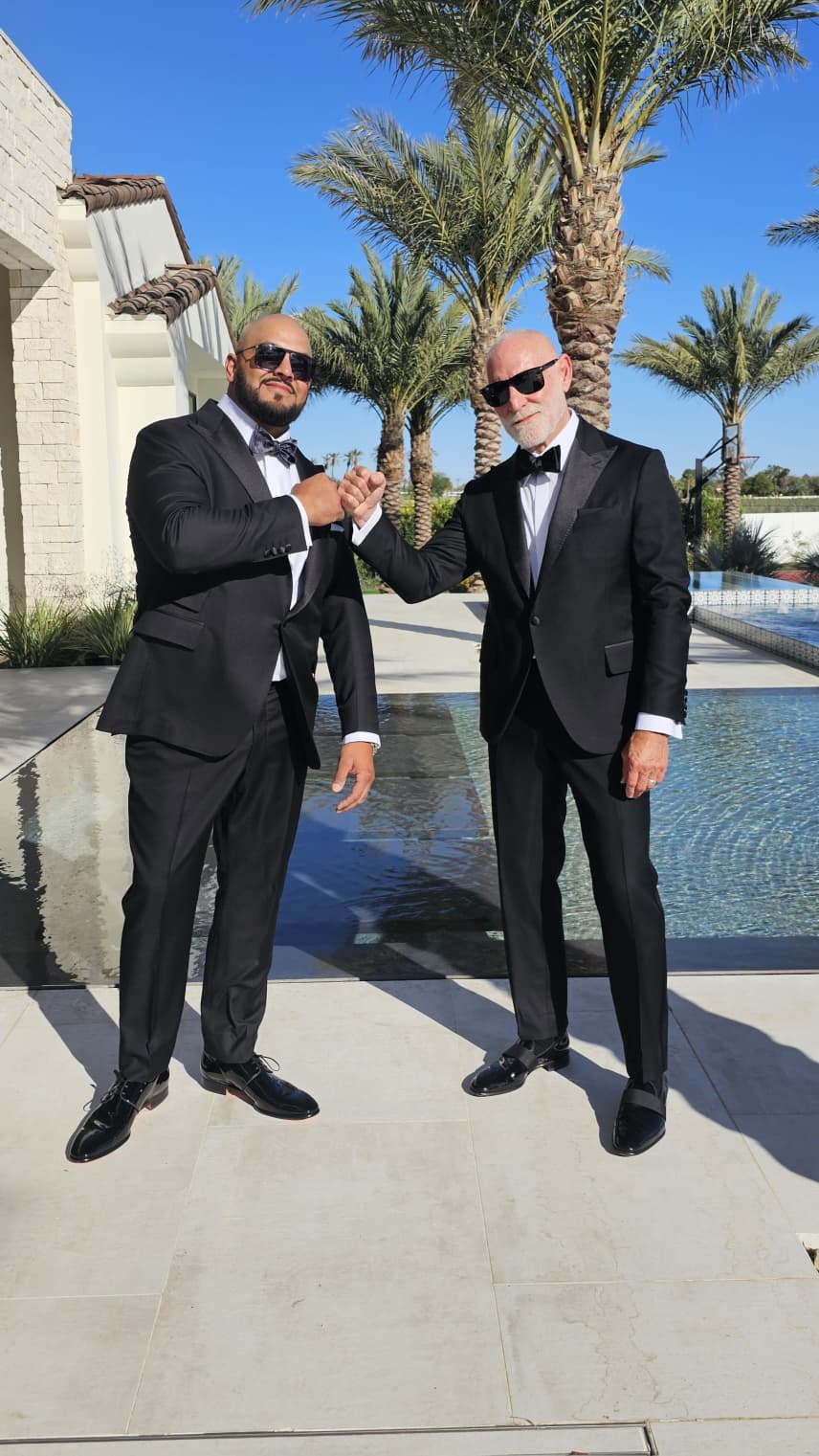 Randy Willard and a man in matching tuxedos sharing a fist bump by a pool