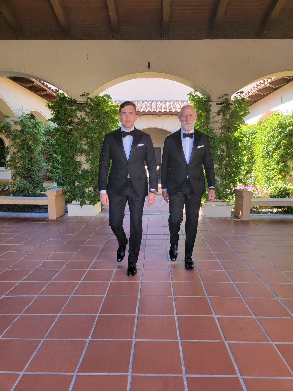 aRandy Willard walking with a client, both in tailored tuxedos