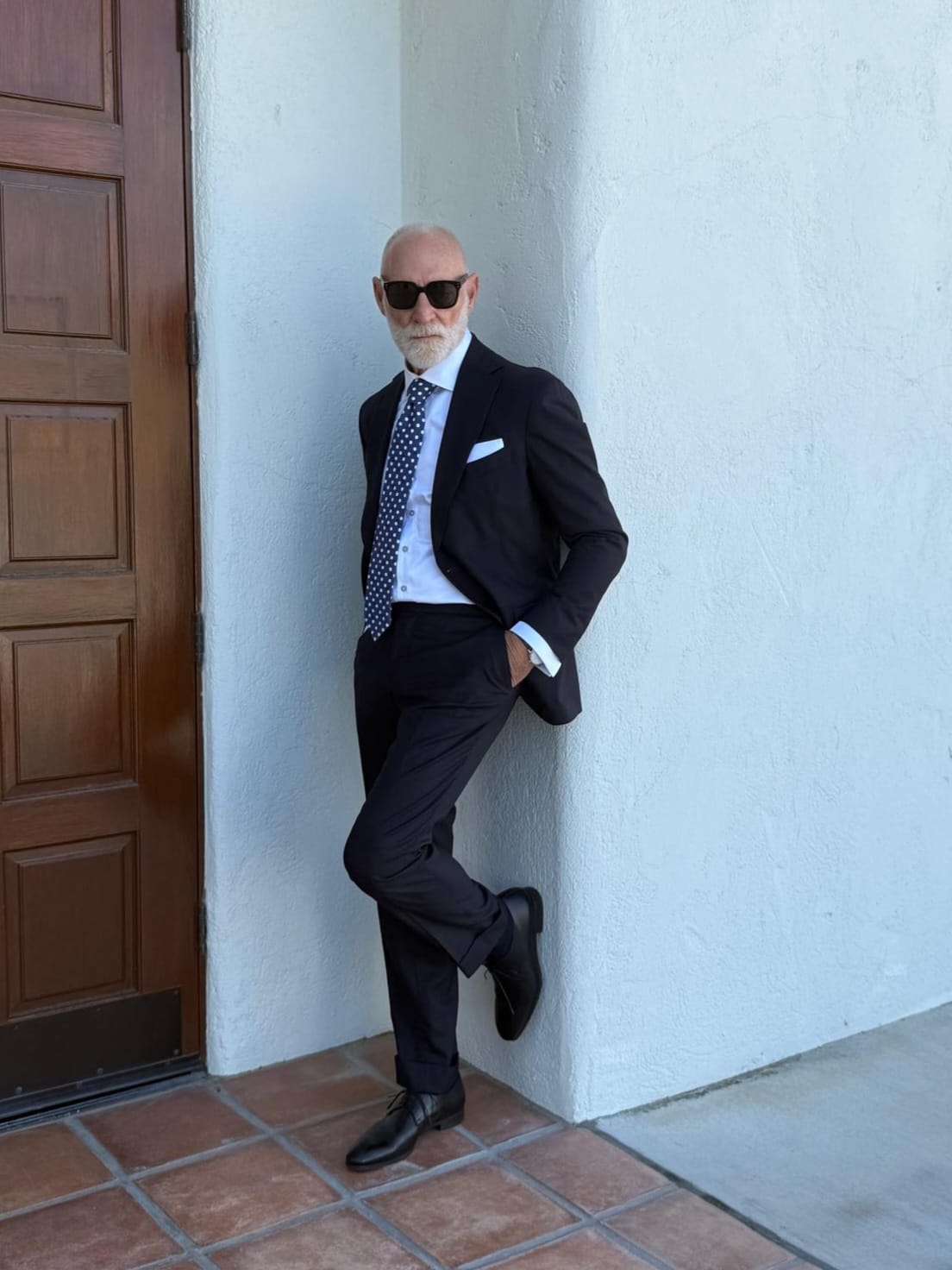 Randy Willard in a navy suit and polka dot tie, leaning against a white wall