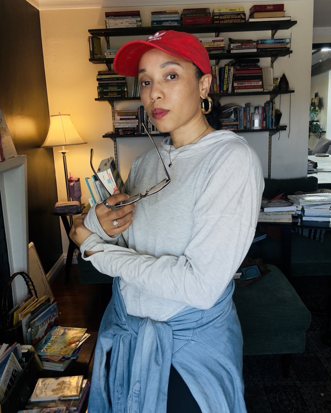 The founder in a red cap, holding books and her glasses in front of a bookshelf