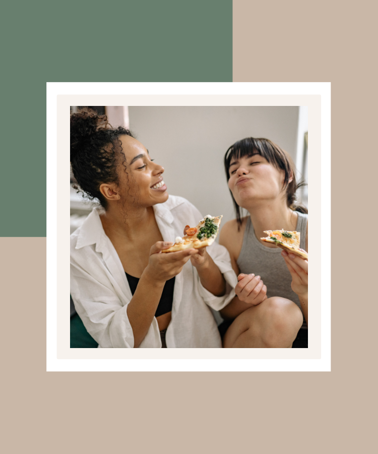 Two women smiling and enjoying pizza together, presented in a white photo frame against a sage green and beige background.