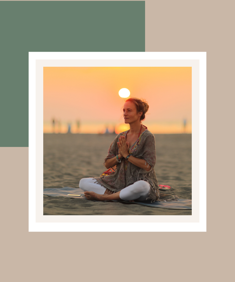 A woman sitting cross-legged on a beach at sunset with her hands together in a peaceful meditation pose, framed against a muted sage green and beige background.