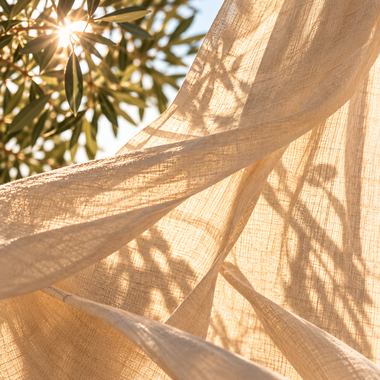Soft beige linen fabric flowing in gentle folds, illuminated by warm golden sunlight filtering through olive branches, creating delicate leaf shadows and a peaceful atmosphere.