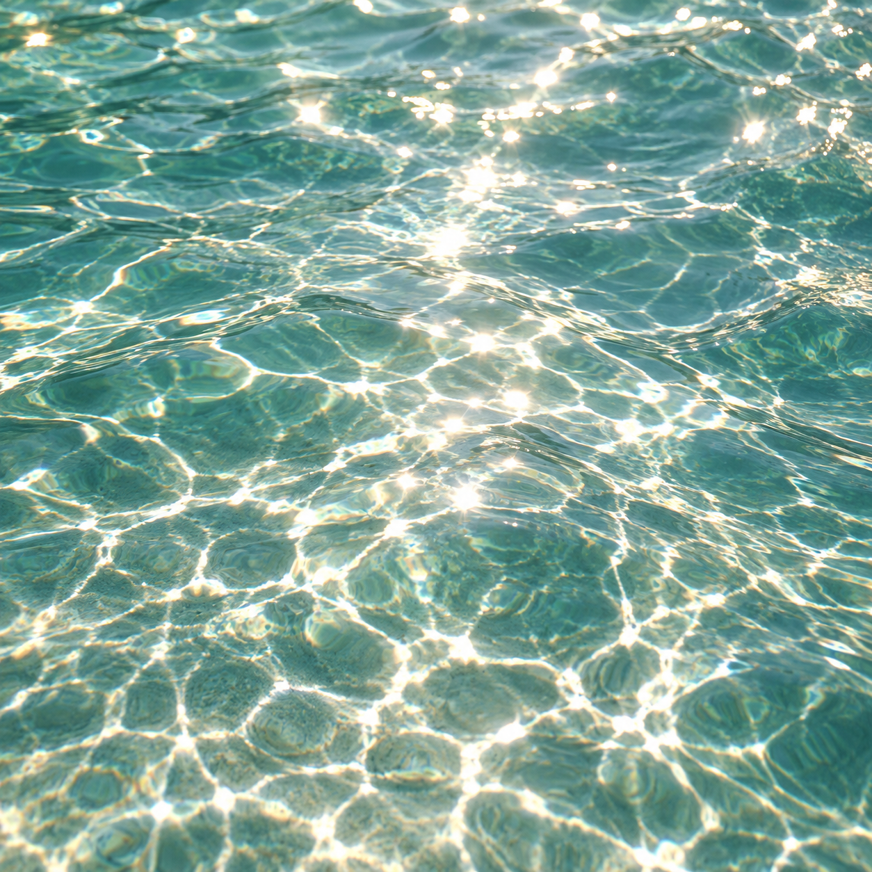 Gentle ripples across clear turquoise water, with golden sunlight sparkling on the surface and creating soft, shimmering reflections.