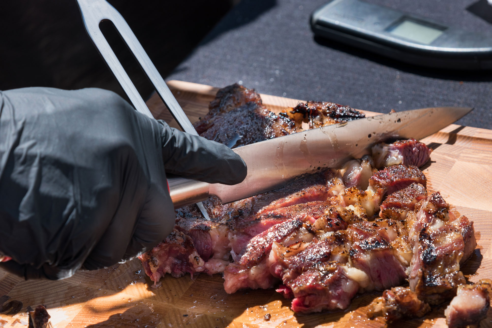 Gloved hand carving slow-cooked beef on a board