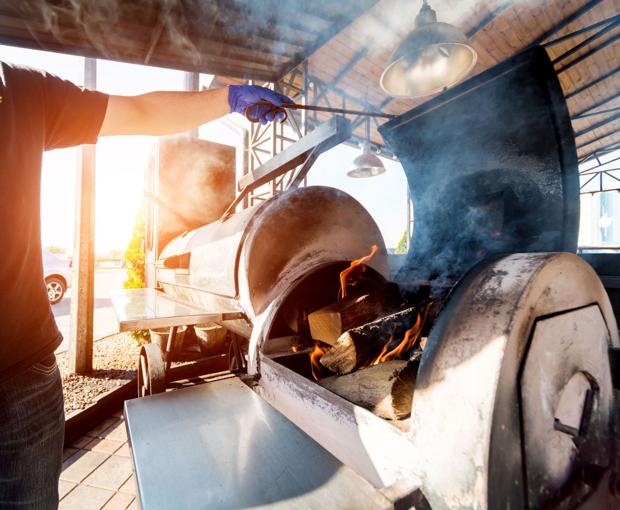 Steel offset smoker open on a covered prep deck, smoke rolling out