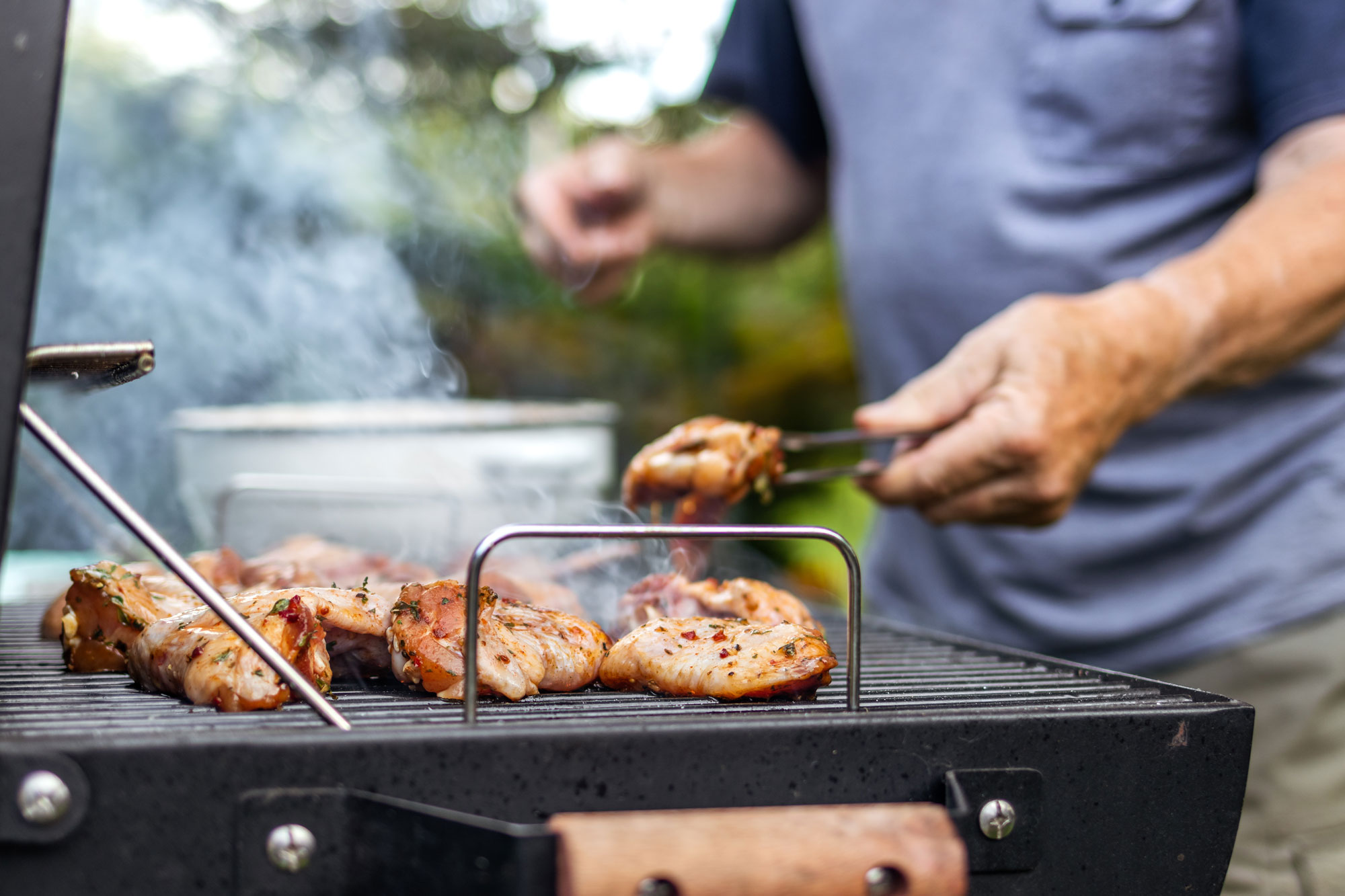 Hands turning chicken on a steel grill