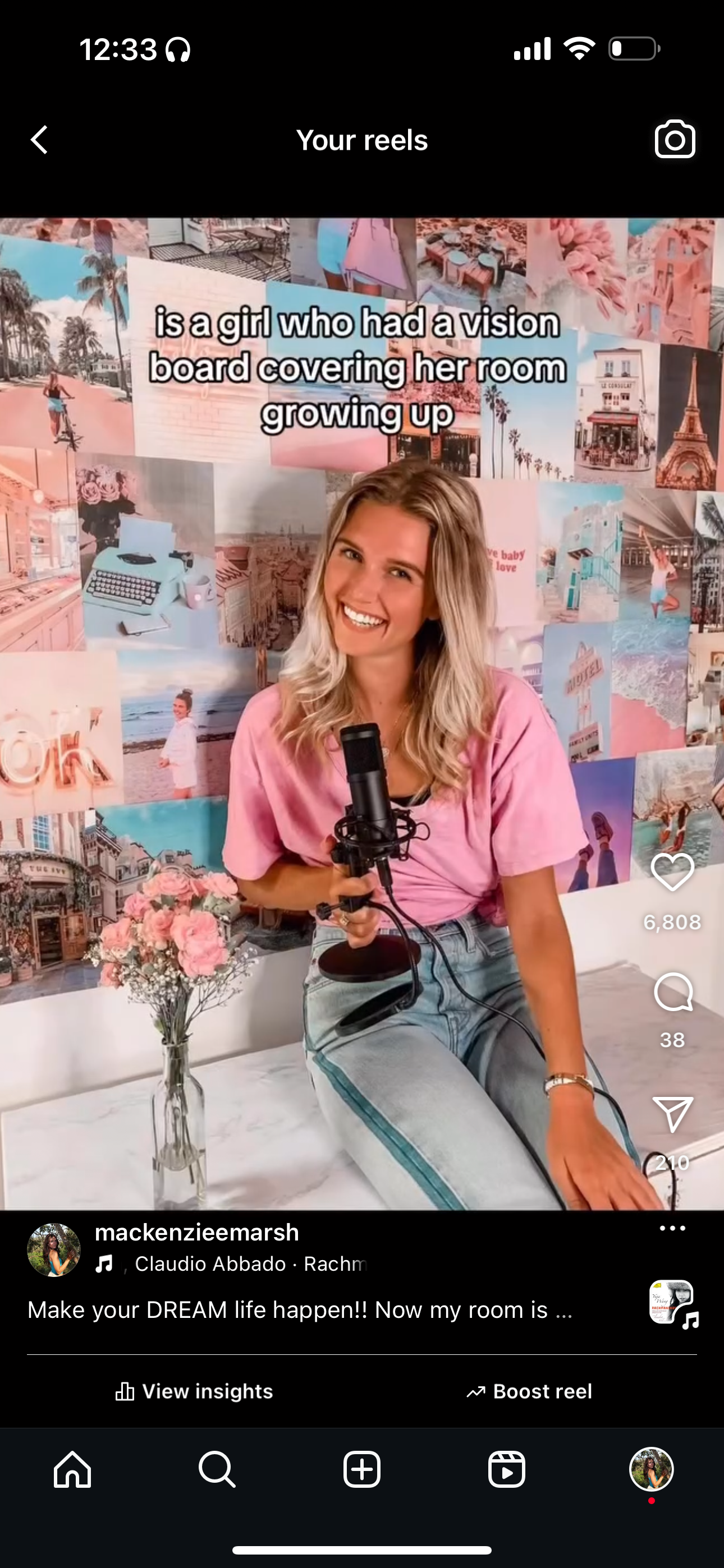 Mackenzie with long blonde hair, holding a podcast mic in front of her vision board wall