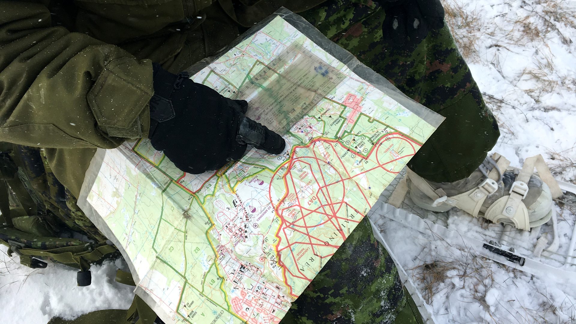 A gloved hand tracing a route on a topographic map in the snow, with snowshoes alongside