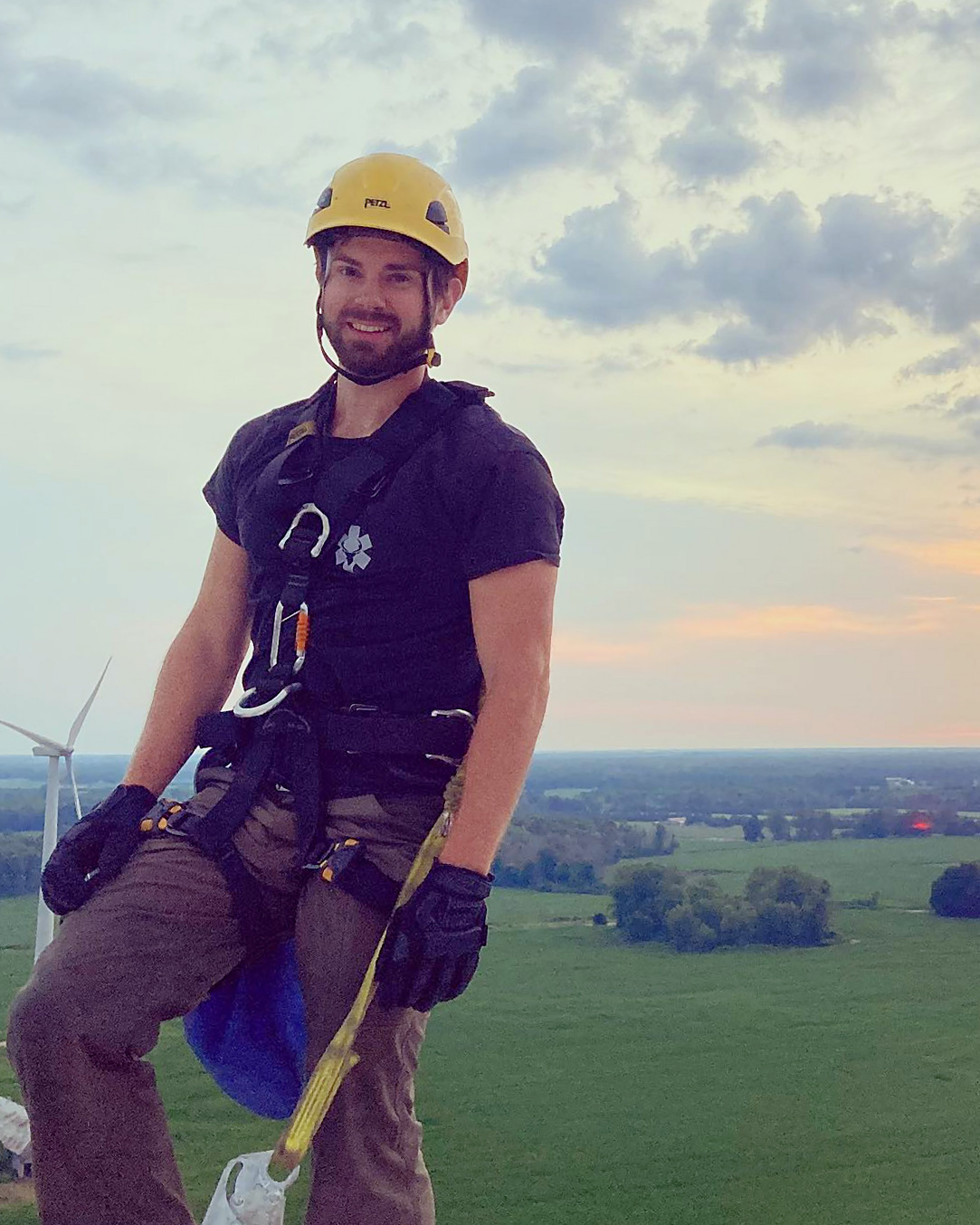 Brandon Nicksy in a rope access harness on top of a wind turbine at sunrise.