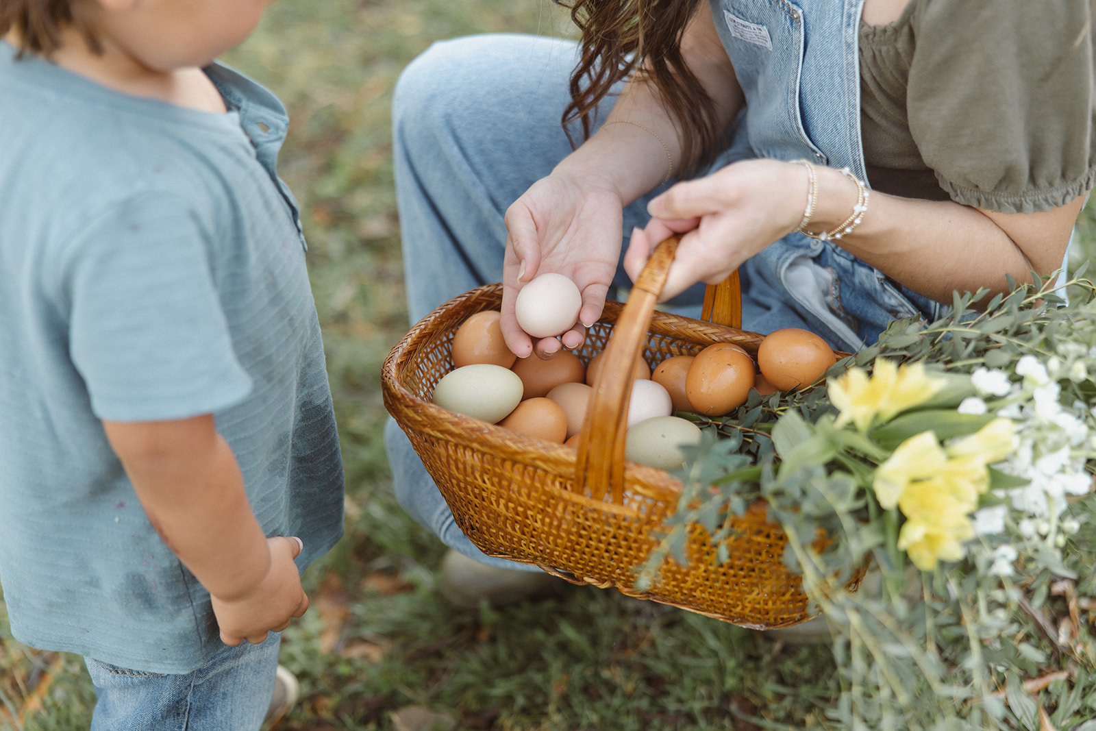 A child gathering eggs into a basket with mom