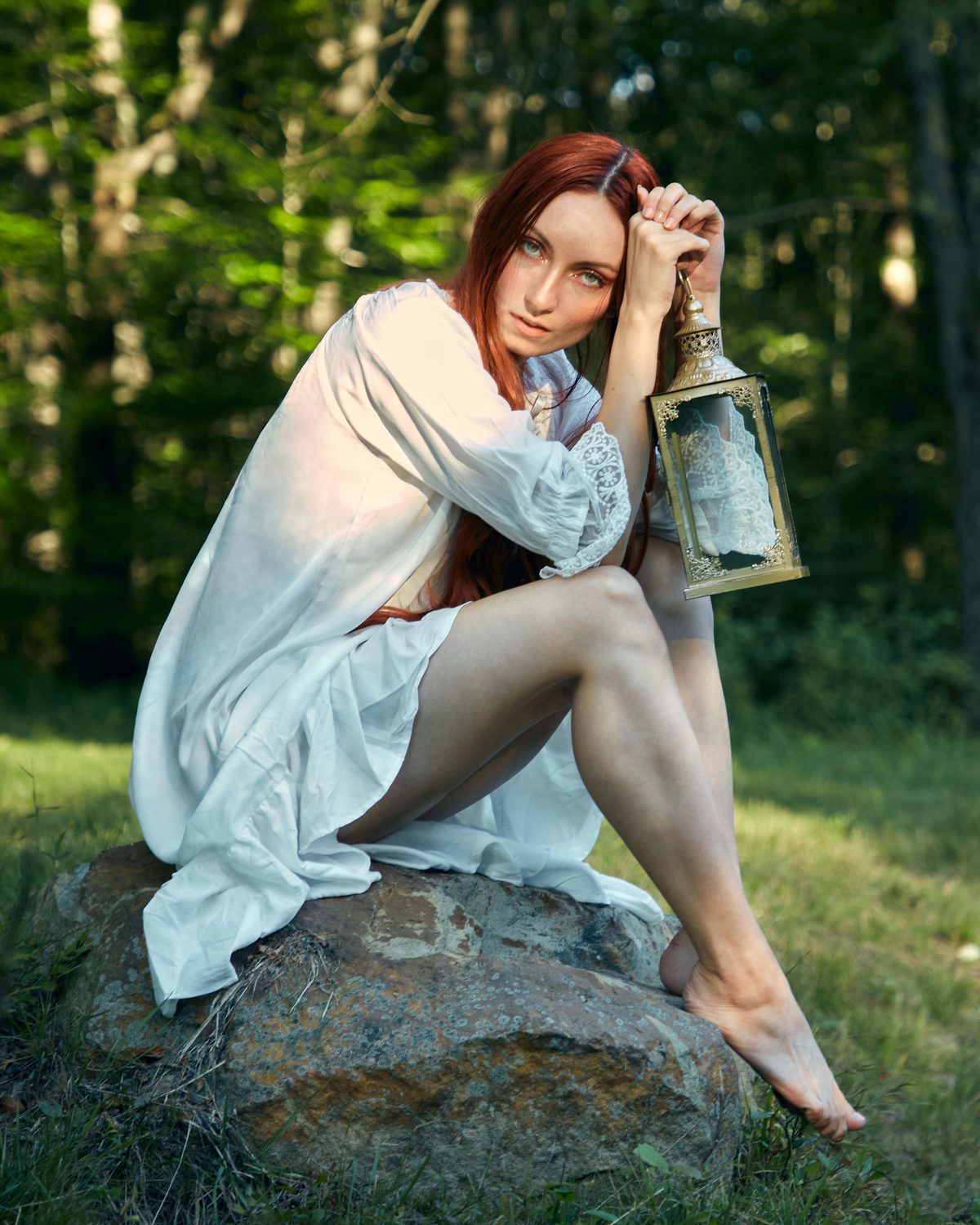 Rocío in a white dress sitting on a mossy rock in a summer forest, holding a lantern